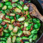 Pan-fried Brussels sprouts with bacon in a black skillet.