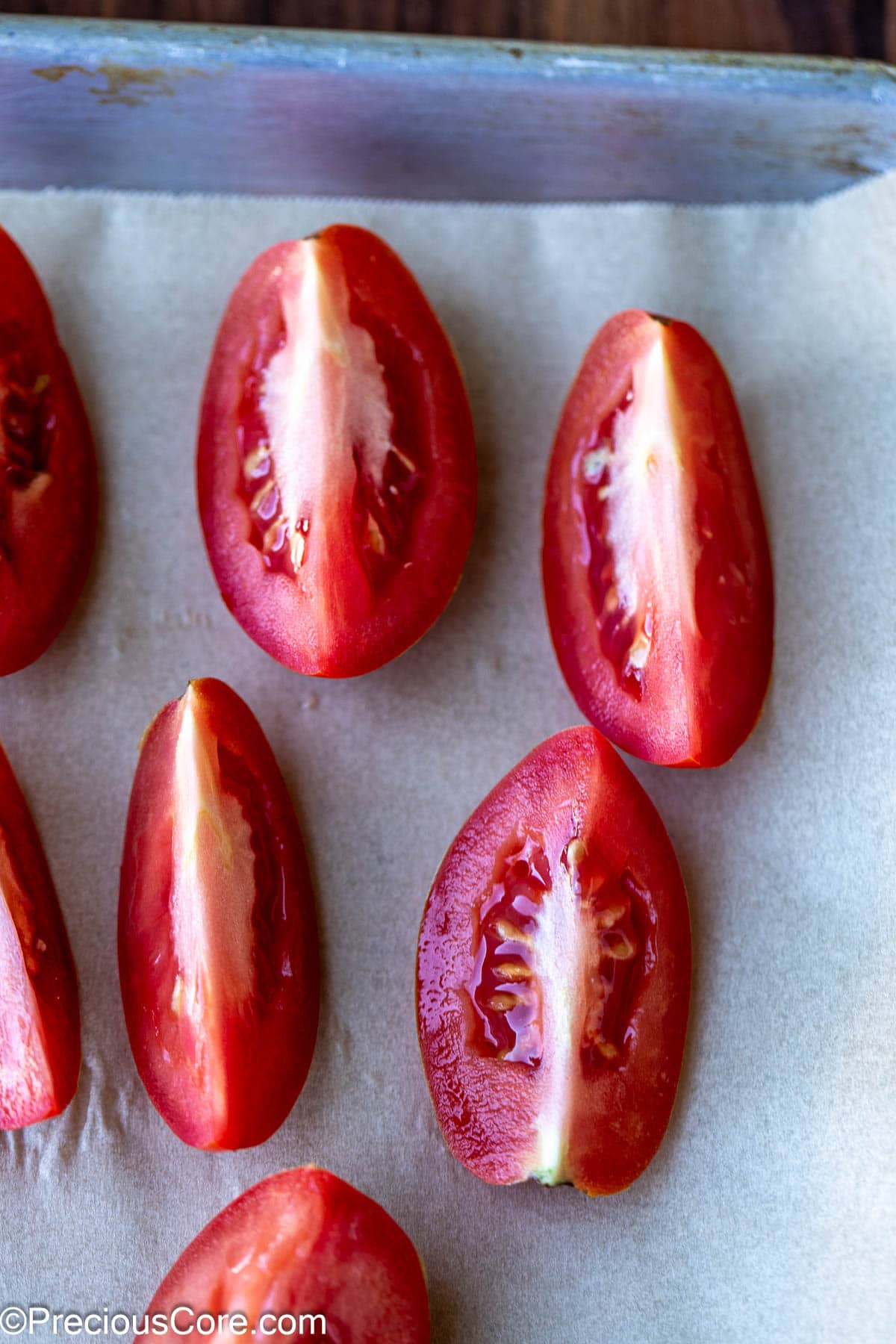 Roma tomatoes cut into quarters on parchment paper.