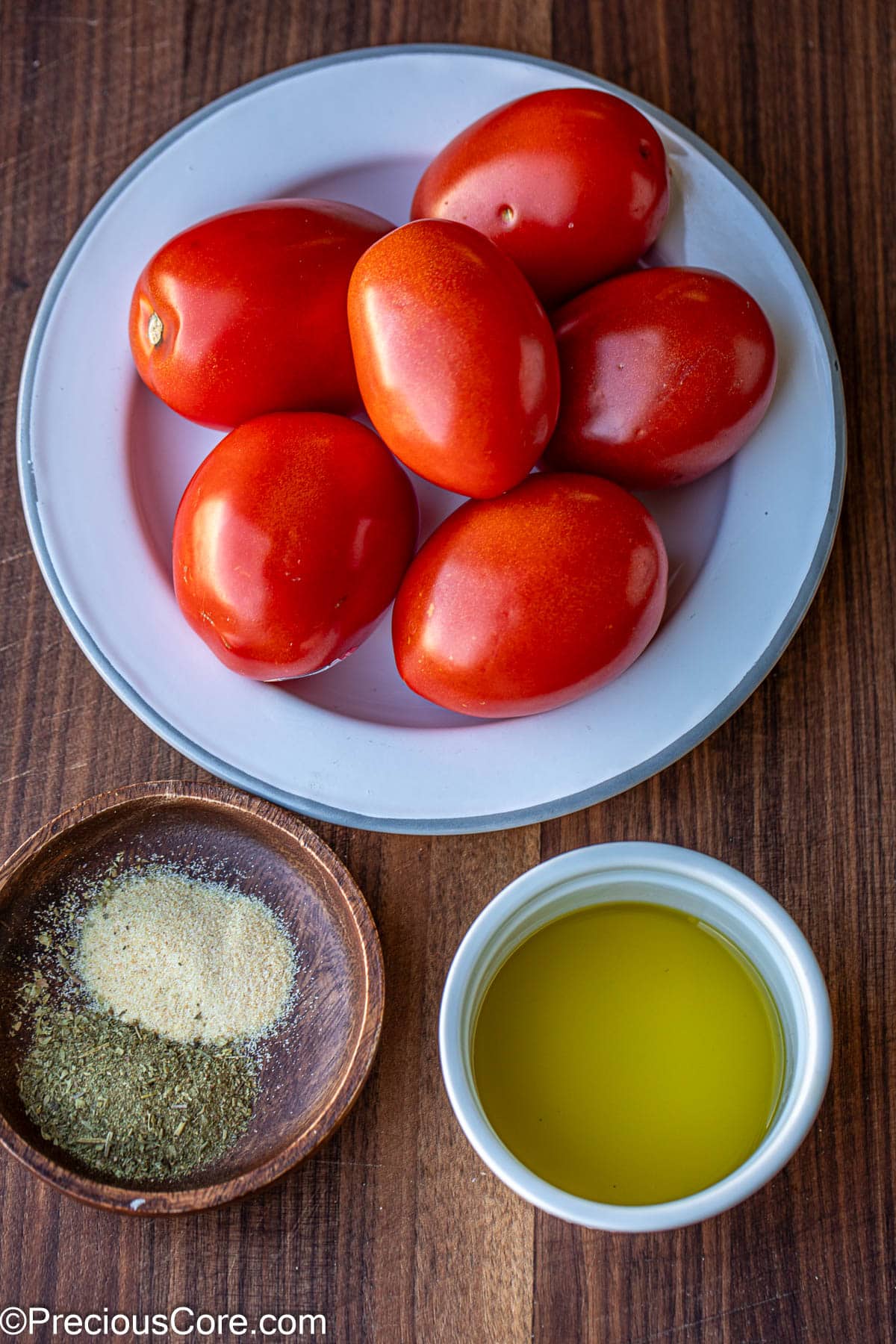 Tomatoes on a white plate, spices in a wooden bowl and oil in a small bowl.