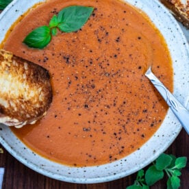 Roasted tomato and garlic soup in a bowl with a grilled cheese sandwich dipping into the soup.