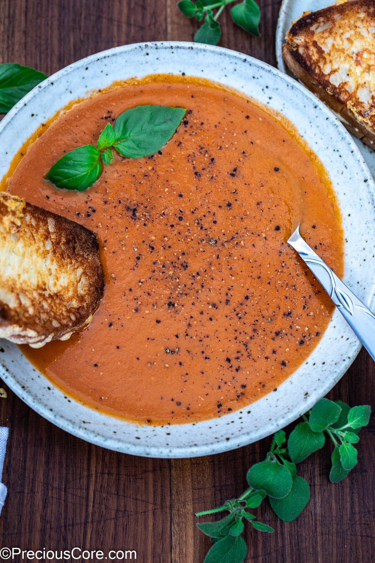 Roasted tomato and garlic soup in a bowl with a grilled cheese sandwich dipping into the soup.