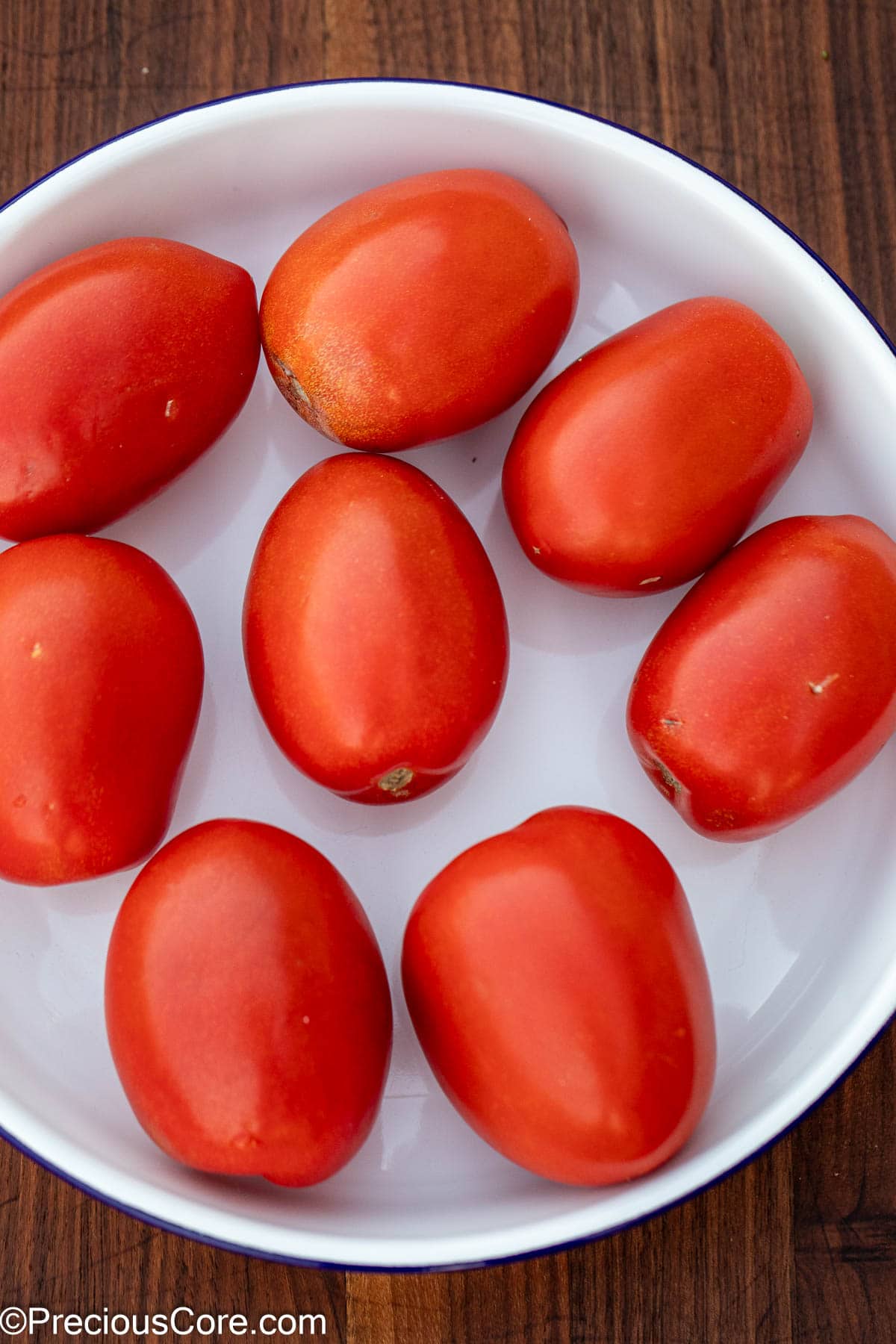 Bright red Roma tomatoes in a white bowl.