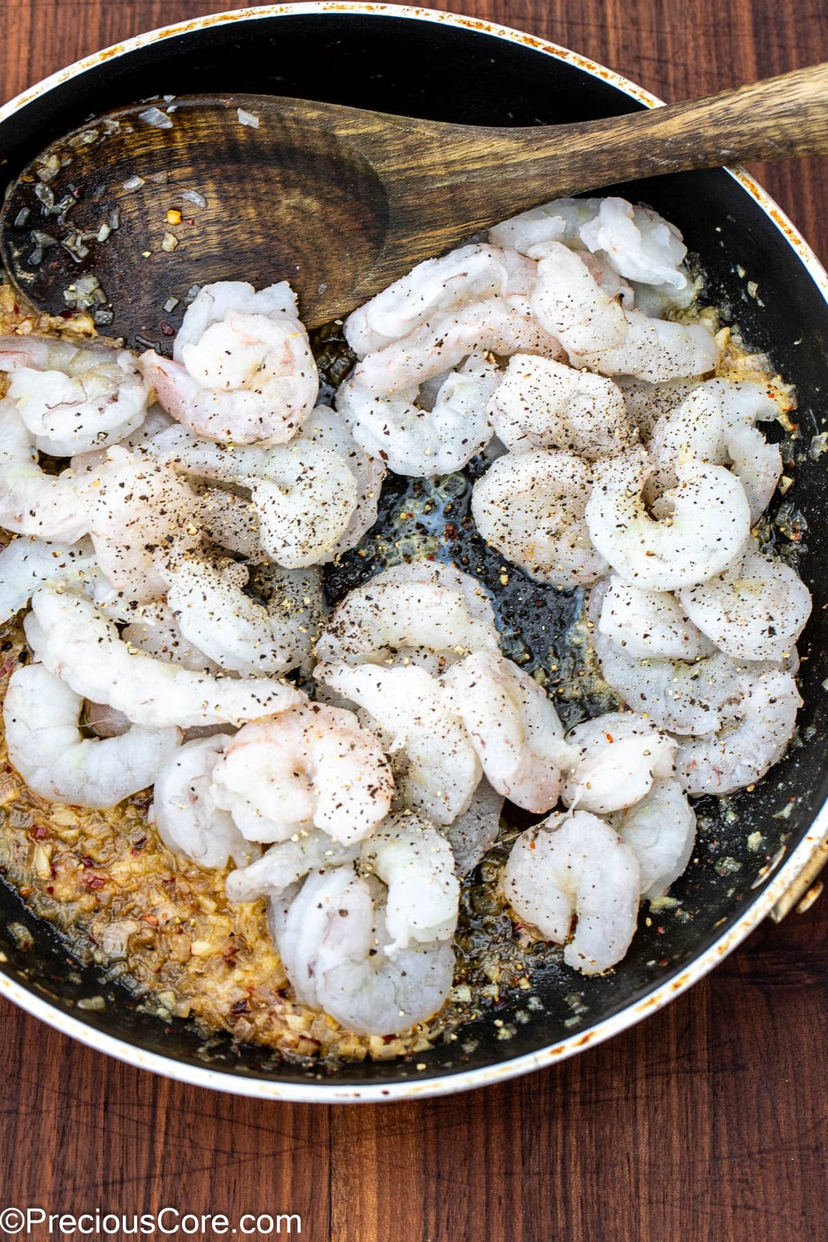 Shrimp in a skillet sprinkled with salt and black pepper.