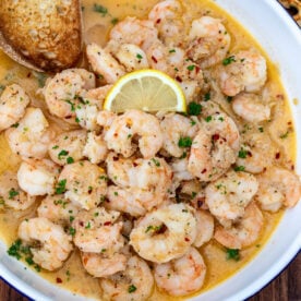 Crusty bread in a bowl of shrimp in white wine sauce.