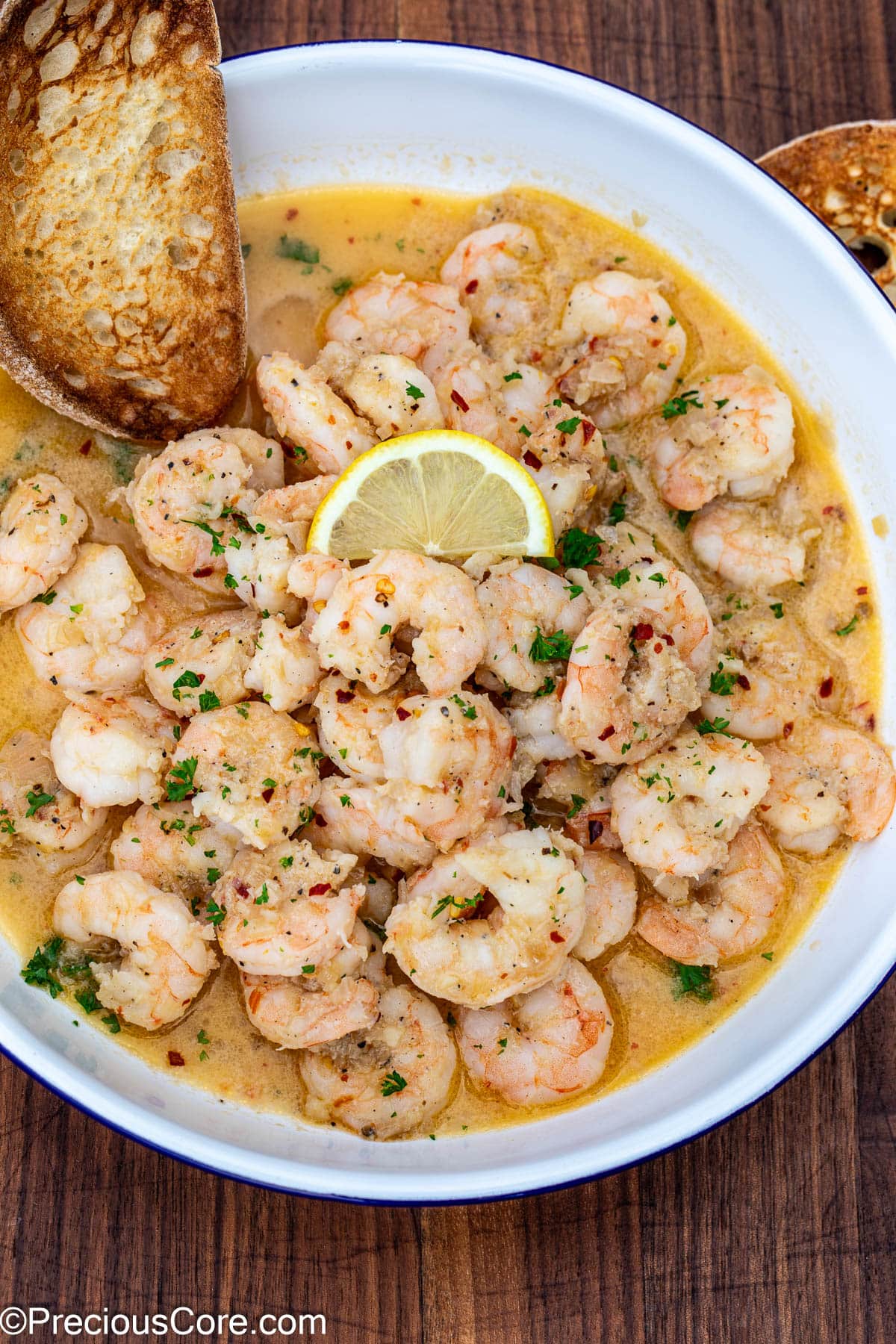 Crusty bread in a bowl of shrimp in white wine sauce.