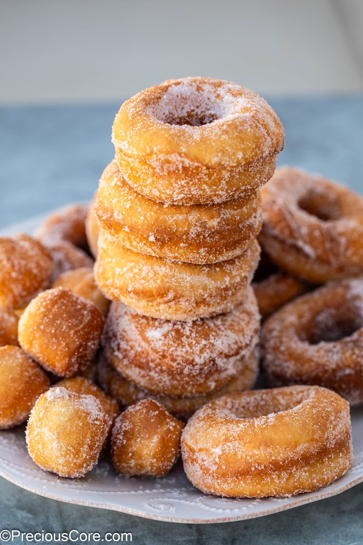 A stack of sugar coated donuts with more doughnuts surrounding it.