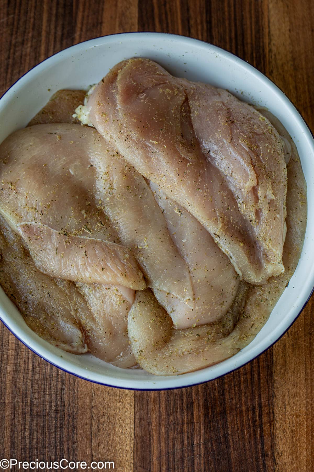 Seasoned chicken breasts in a white bowl.