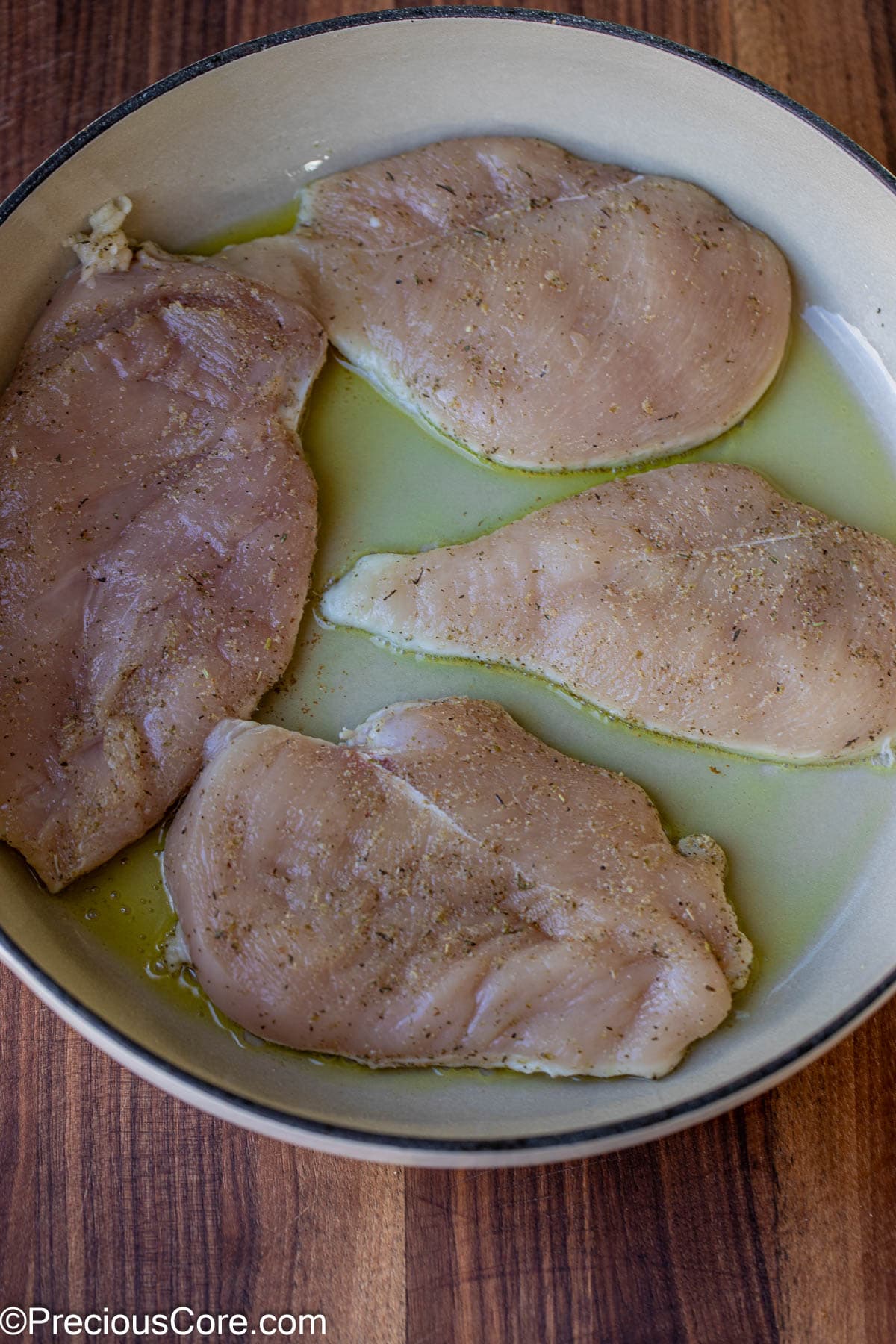 Raw seasoned chicken breasts added to a pot with olive oil.