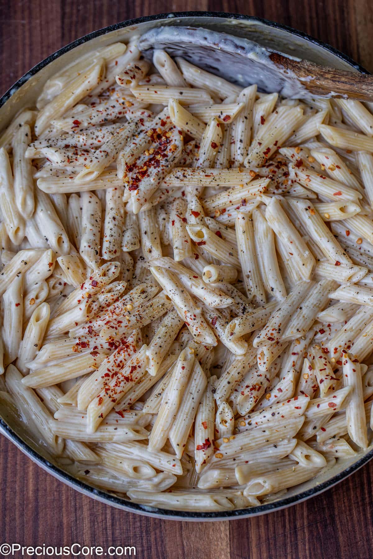 A pot of creamy penne sprinkled with crushed pepper flakes and black pepper.