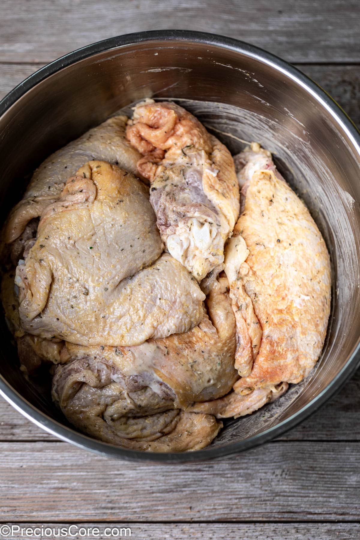 Seasoned chicken thighs in a stainless steel mixing bowl.