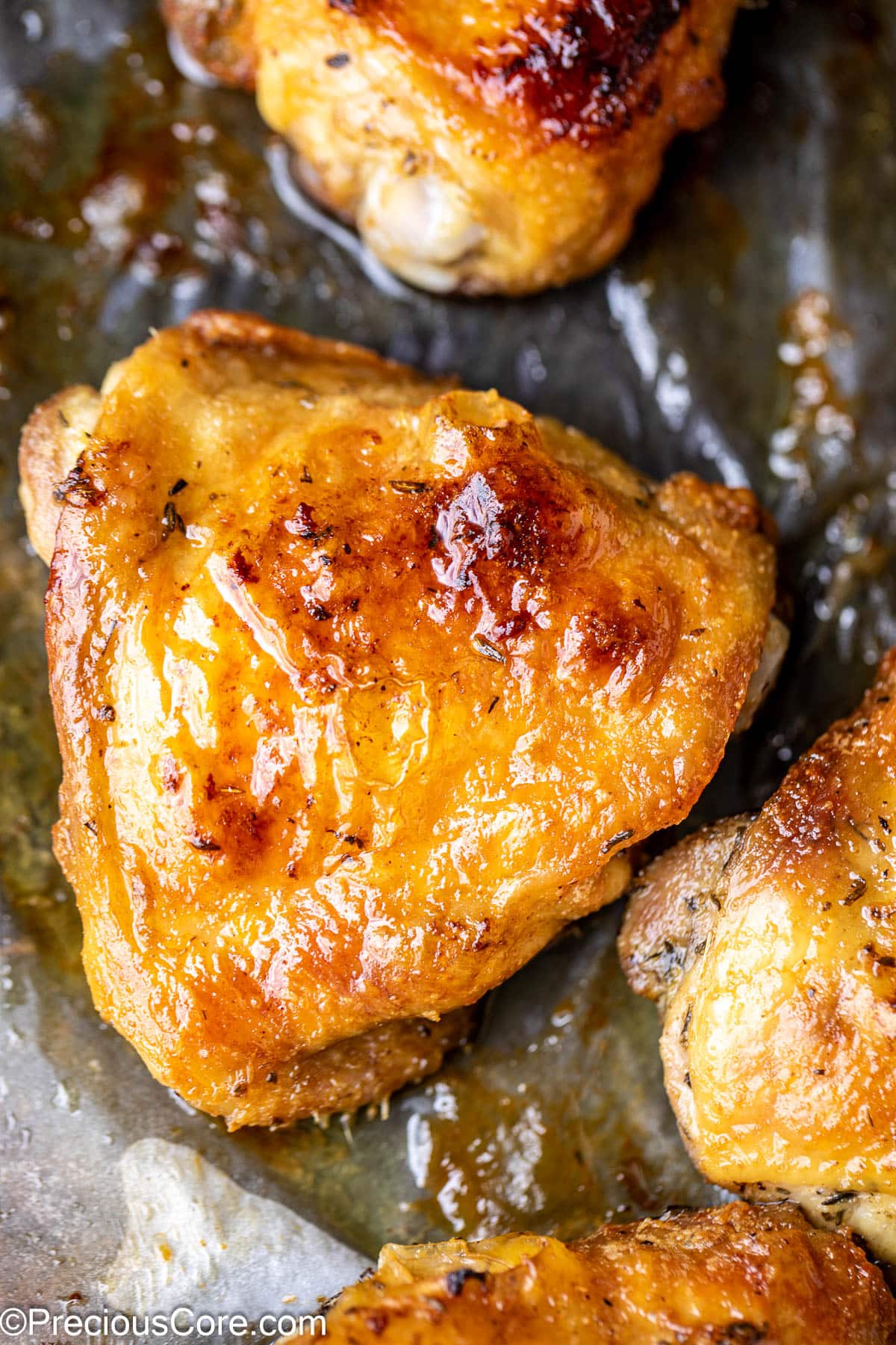 Close up on a glistening golden brown chicken thigh on parchment paper.