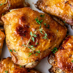 Close up on a golden brown chicken thigh, surrounded by other chicken thighs.