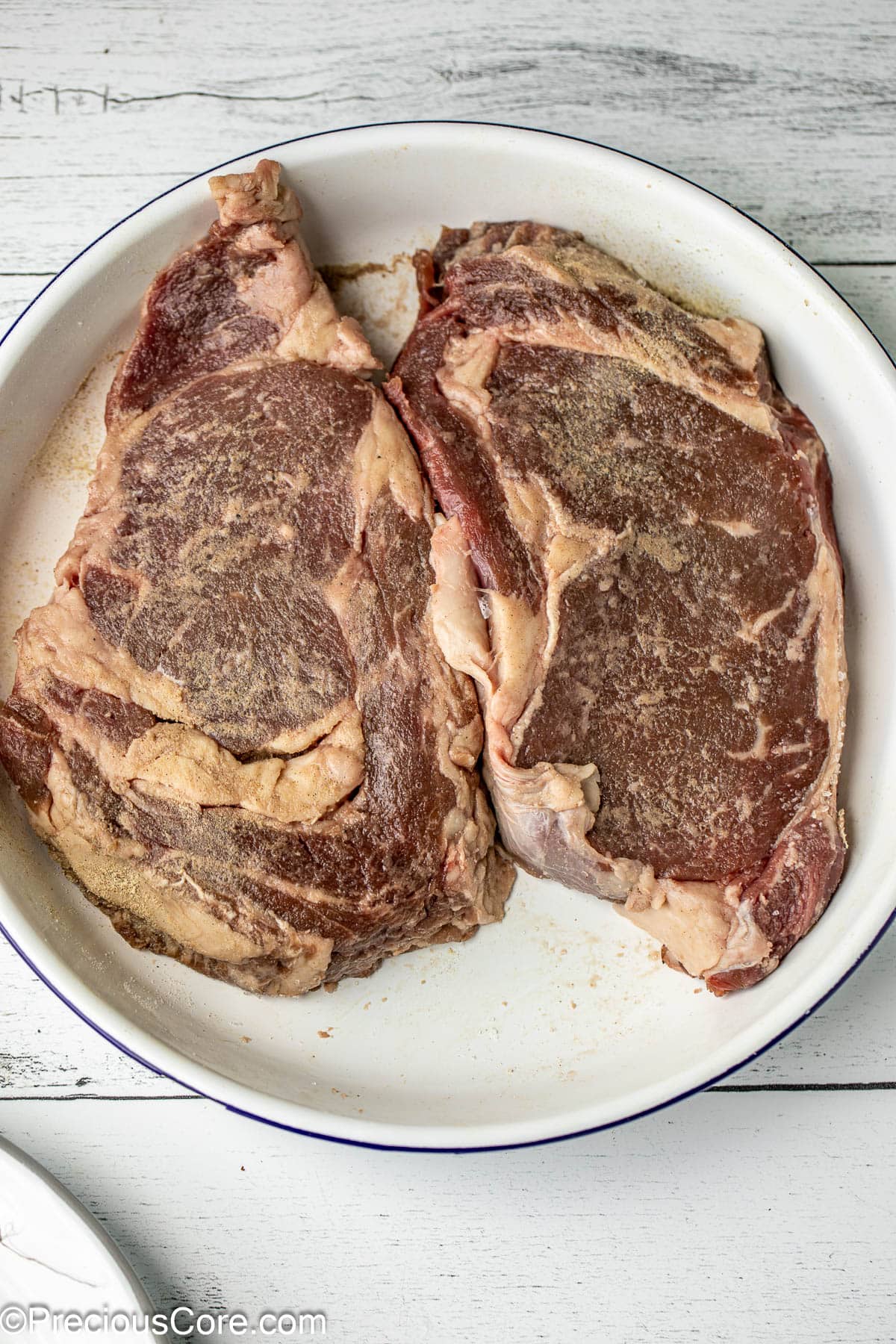 2 seasoned steaks in a white bowl.